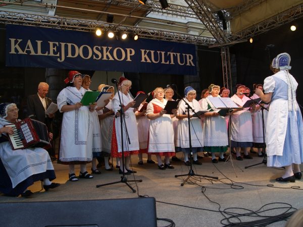 Zdjęcie przedstawia uczestników festiwalu Kalejdoskop Kultur, na scenie stoją kobiety w strojach ludowych, z tekstem pieśni w rękach.