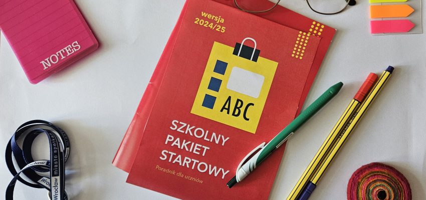 Zdjęcie przedstawia publikację oraz przedmioty związane skojarzeniowo ze szkołą leżące na stole i sfotografowane z góry. Wsód przedmiotów jest notes, smycz, długopisy, okulary i karteczki post-it.