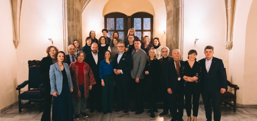 Kilkonaścioro osób w różnym wieku, ubranych elegancji, stoi na tle portalu gotyckiego we wrocławskim Ratuszu.