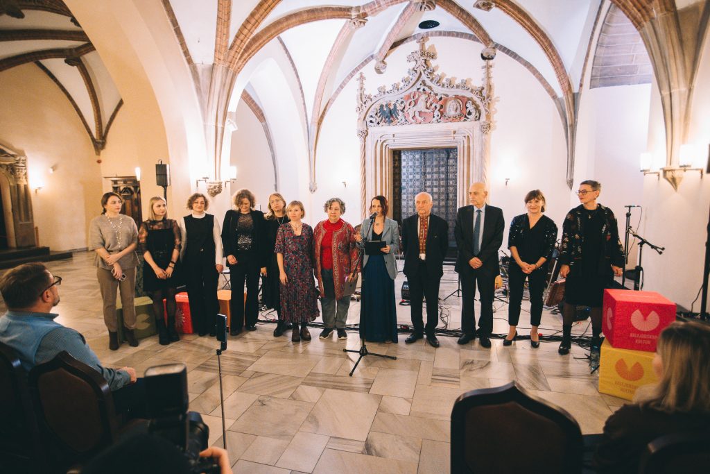 Kilkonaścioro osób w różnym wieku, ubranych elegancji, stoi na tle ozdobnych drzwi we wrocławskim Ratuszu.