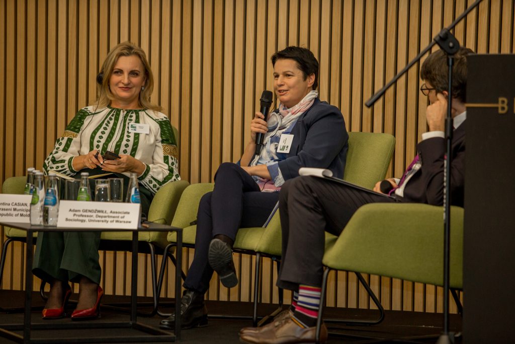 Zdjęcie przedstawia dwie kobiety i mężczyznę siedzących w fotelach na panelu dyskusyjnym. Kobieta w środku trzyma mikrofon.