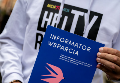 zdjęcie przedstawia tors osoby w jasne bluzie, która trzyma publikację "Informator Wsparcia"