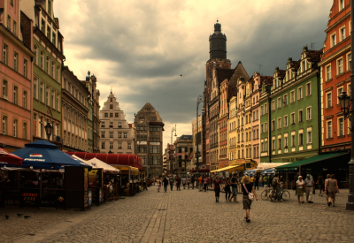 Zdjęcie przedstawia rynek Starego Miasta we Wrocławiu, sfotografowany z perspektywy ulicy, po lewej i po prawej stronie znajdują się kamieniczki, wzdłuż nich ogródki restauracyjne.
