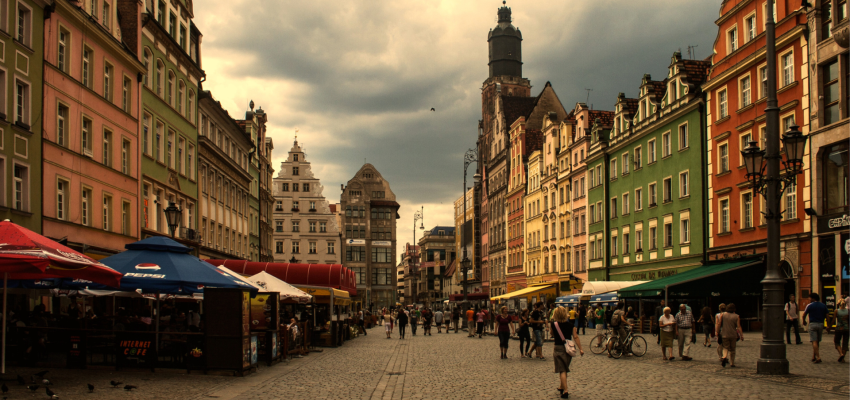 Zdjęcie przedstawia rynek Starego Miasta we Wrocławiu, sfotografowany z perspektywy ulicy, po lewej i po prawej stronie znajdują się kamieniczki, wzdłuż nich ogródki restauracyjne.