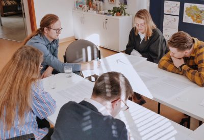 Pięć osób siedzi przy stoliku, na którym rozłożone są dokumenty